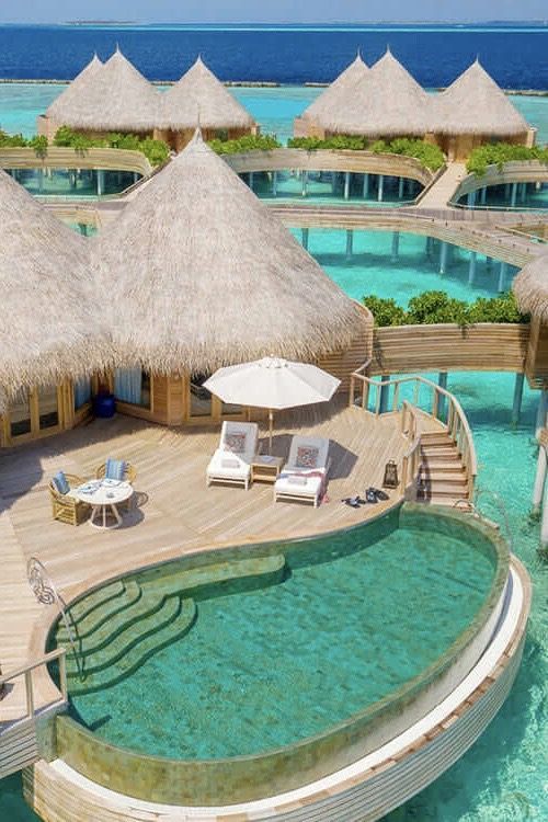 an over water pool with thatched umbrellas and lounge chairs on the deck next to it