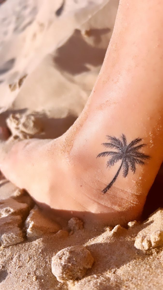 a small palm tree tattoo is on the foot of a person's feet at the beach