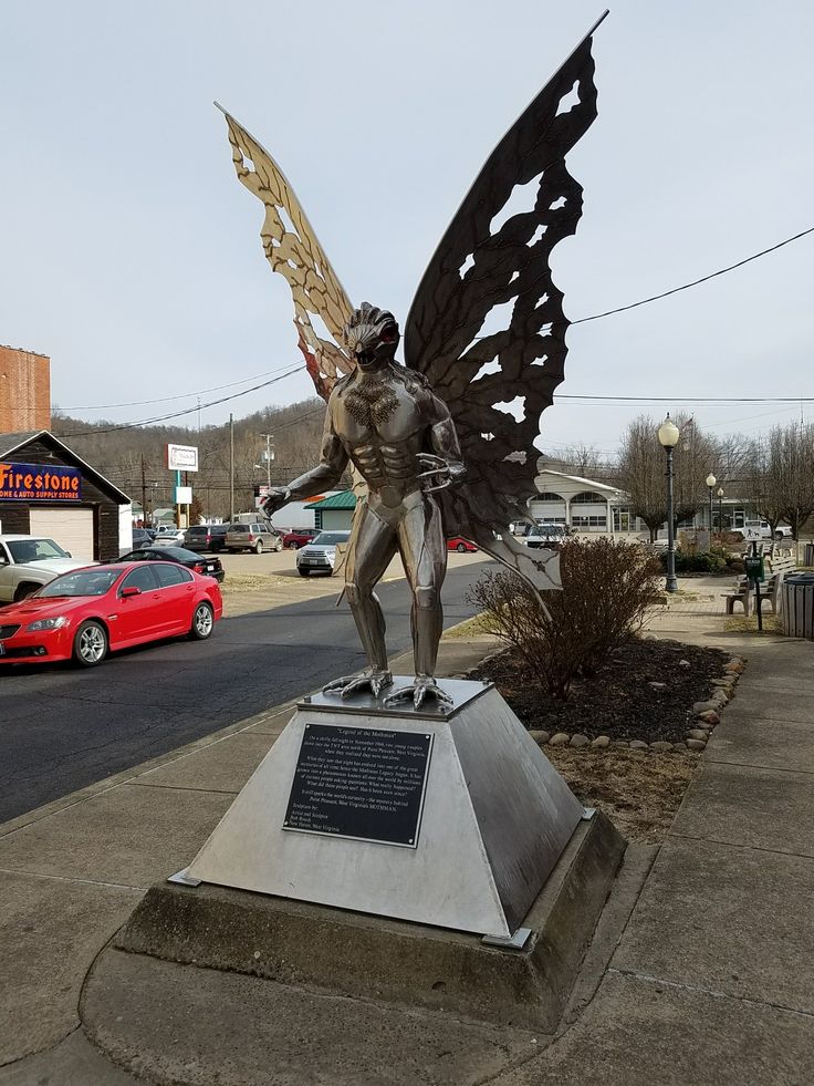 a statue of a man with wings on a pedestal in front of a red car