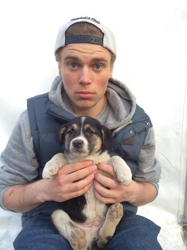 a man holding a small dog in his lap while wearing a baseball cap and jacket