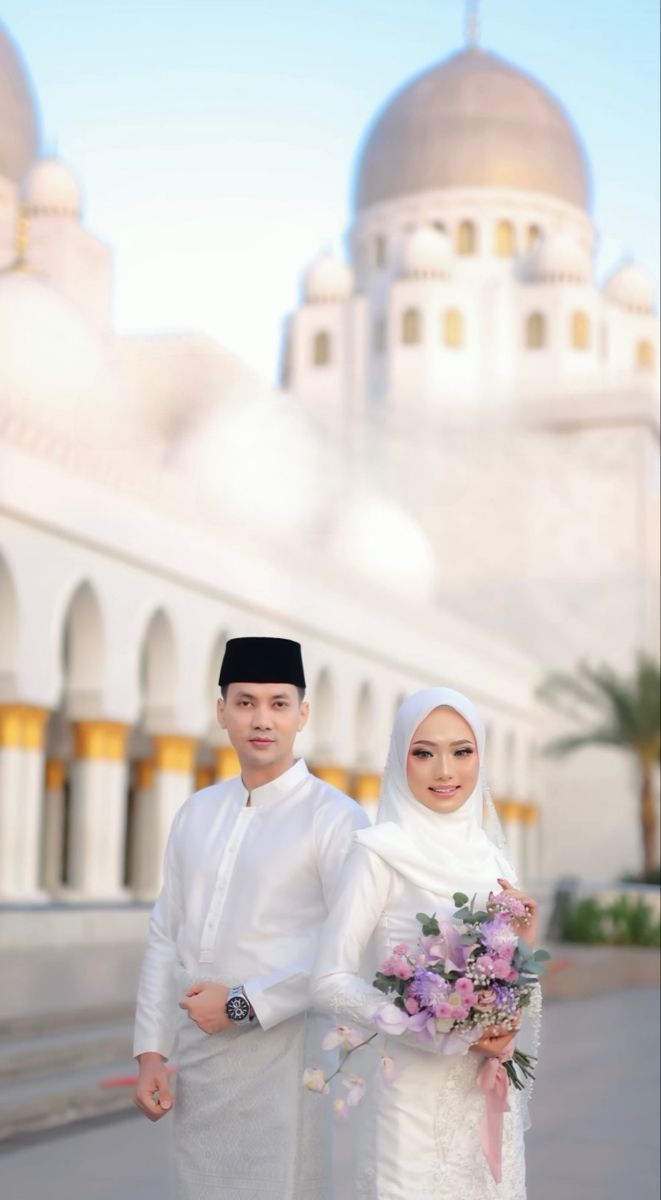 two people standing next to each other in front of a white building with arches and domes