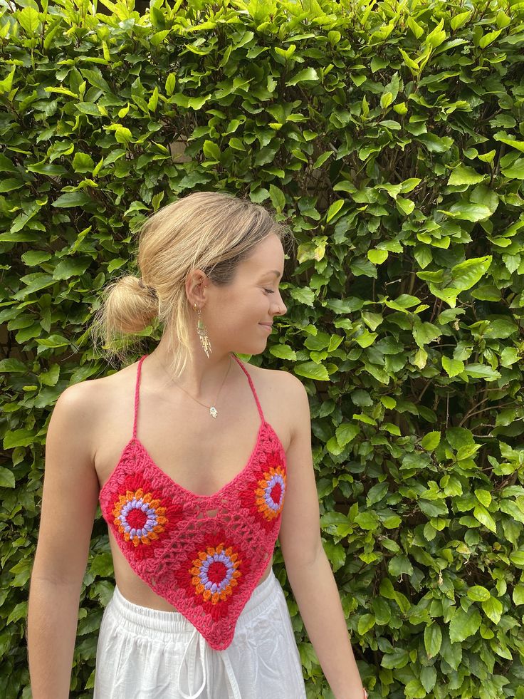 a woman standing in front of a hedge wearing a crocheted top and white shorts