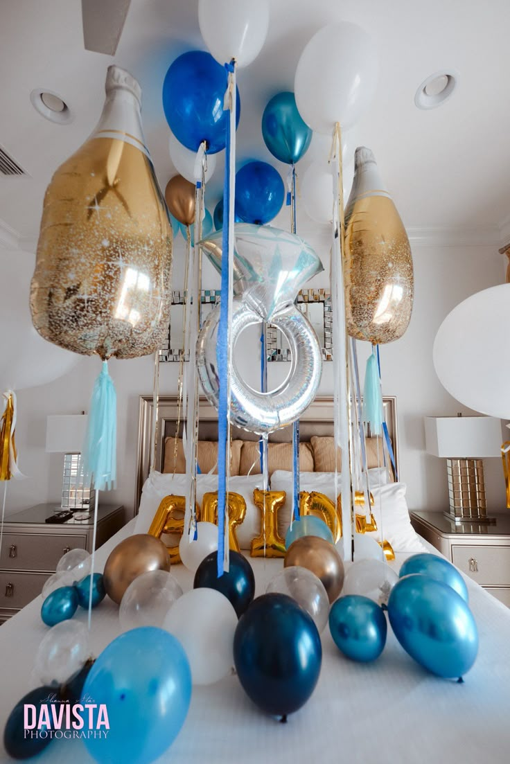 balloons and streamers are hanging from the ceiling above a bed in a room with white walls