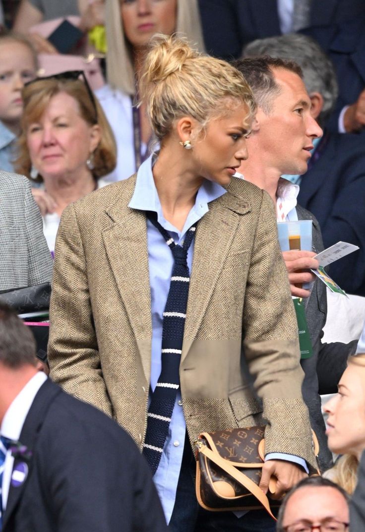 two women in suits and ties are walking together at a sporting event with people behind them