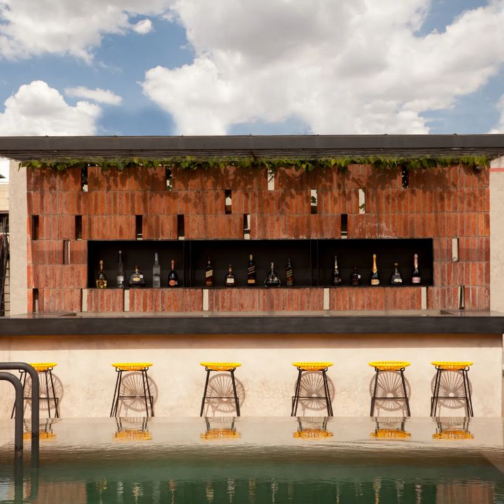 an outdoor bar with yellow stools next to the water in front of a building