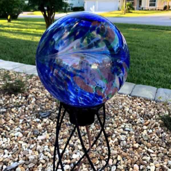 a blue ball sitting on top of a metal stand in the middle of a gravel field