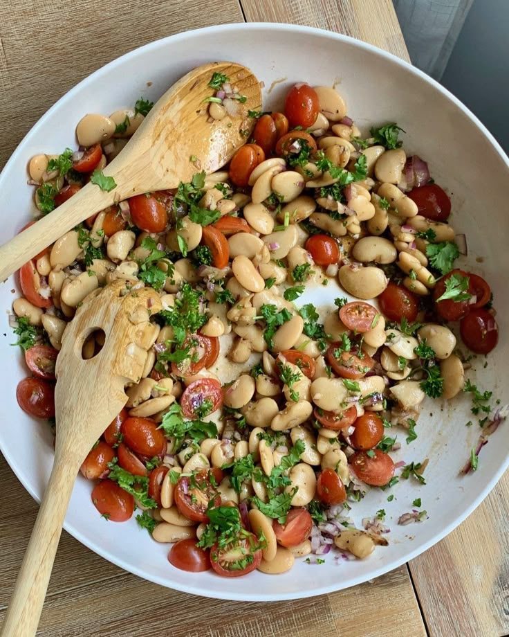 a white bowl filled with beans, tomatoes and parsley on top of a wooden table