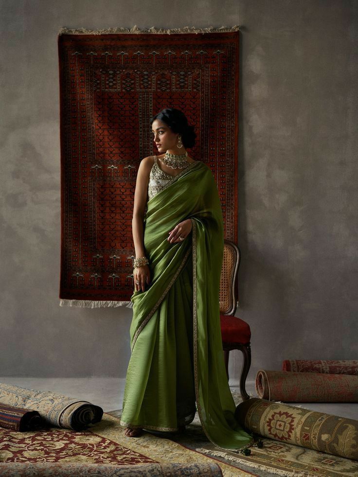 a woman in a green sari standing next to rugs and an old chair