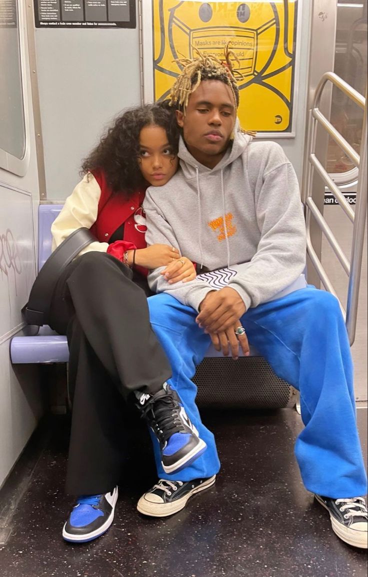 a man and woman sitting on a subway train seat with their arms around each other