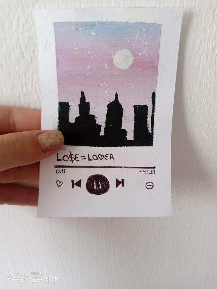 a person holding up a piece of paper with the city skyline painted on it's side