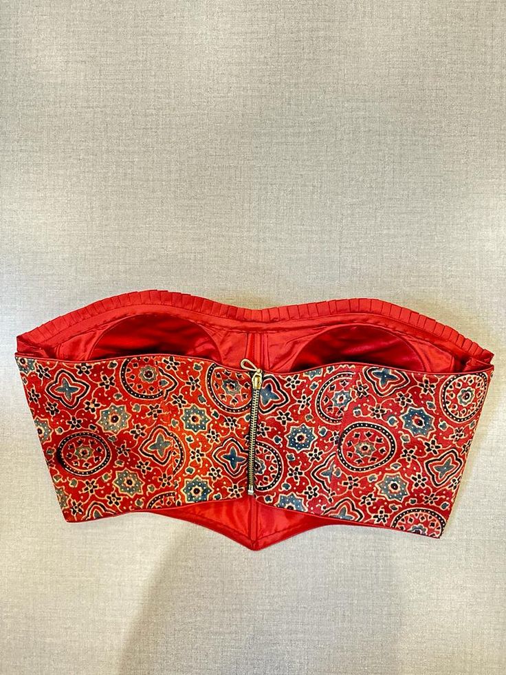 Beautiful red Ajrakh print corset blouse with ruffle detailing. Buy designer blouse in USA from Pure Elegance. Disclaimer: The actual product may vary slightly from the image. These are custom orders, hence expect slight variation in color, placement of the motif or buta. ESTIMATED DELIVERYBecause this is a custom order, it would take about 4 weeks from the date of purchase. RETURN POLICY: This product is a custom order and cannot be returned or exchanged. Ajrak Blouse, Designer Saree Blouse, Indian Clothing Store, Blouse Designer, Corset Blouse, Saree Style, Readymade Saree, Embroidered Saree, Saree Blouses