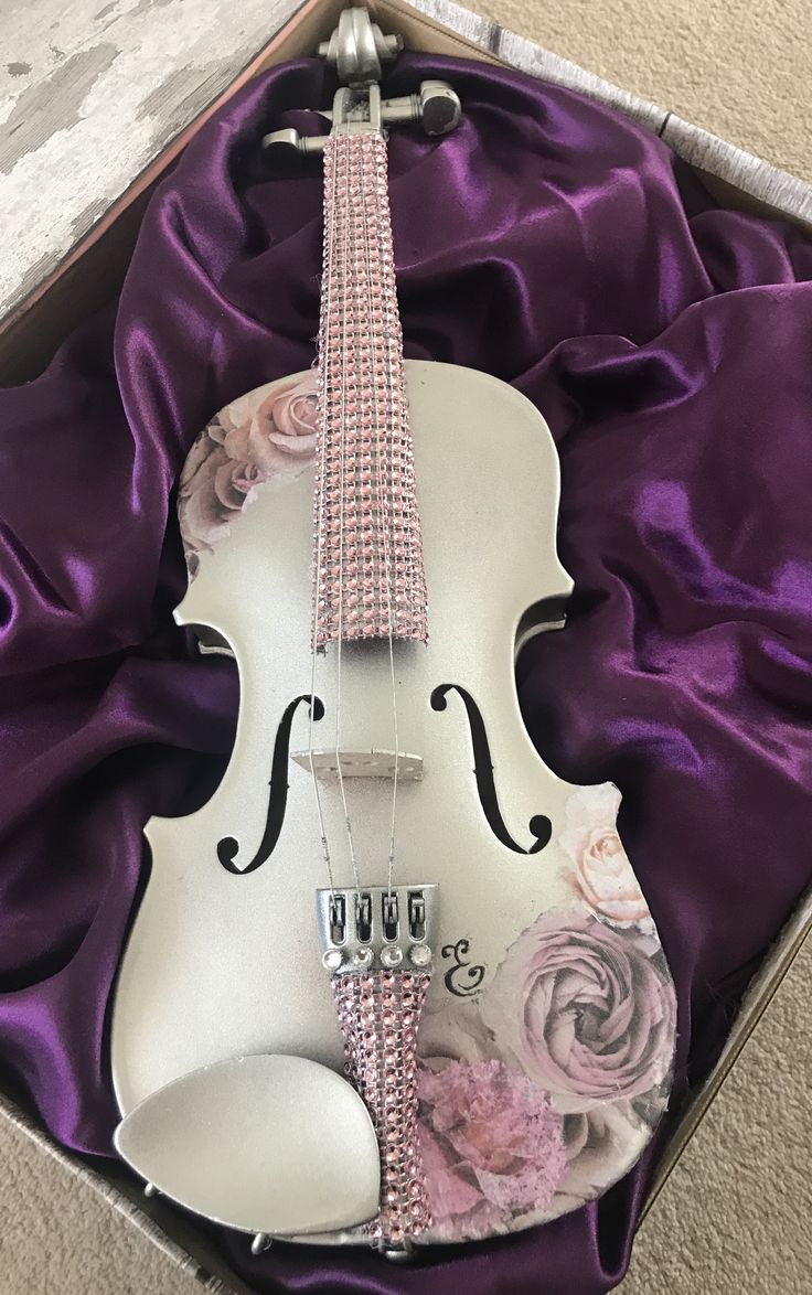 a violin in a box with purple satin and flowers on the bottom, along with other items