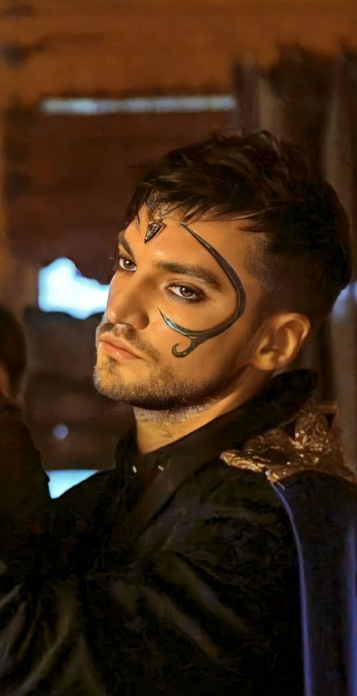 a man with his face painted in black and gold, standing next to a wooden structure