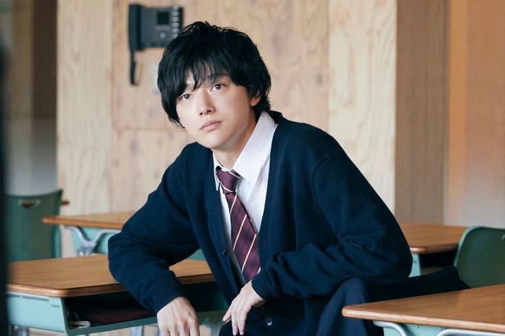 a young man sitting at a desk in a classroom