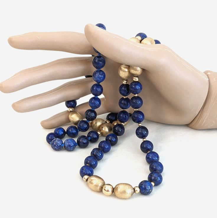 A 36 inch long, lapis lazuli 14 karat gold (tested) beaded necklace.  There is individual knotting between the beads that are to be worn behind the neck.  The lapis beads measure about 10 millimeters in diameter.  There are four sizes of gold beads.  The largest 10 are elongated with a brushed finish, they measure 14 x 10mm.  The other gold beads are round with a polished finish.  There are five 7.5mm, 10 4.5, and 32 3mm beads.  The necklace weighs 106.3 grams.  There are no hallmarks. CONDITION:  The stringing cord is slightly stretched in a few areas of the back section.  A few tiny, shallow dents on the larger gold beads.  No chips or cracks found in the lapis beads. Gold Jewelry With Hand-knotted Round Beads, Gold Double Strand Hand-strung Jewelry, Blue Lapis Lazuli Jewelry With Large Beads, Adjustable Single Strand Lapis Lazuli Necklace, Blue Hand Knotted Jewelry For Gift, Blue Hand-knotted Jewelry For Gift, Single Strand Lapis Lazuli Round Bead Jewelry, Elegant Beaded Necklaces With Round Lapis Lazuli Beads, Elegant Lapis Lazuli Beaded Necklaces With Round Beads