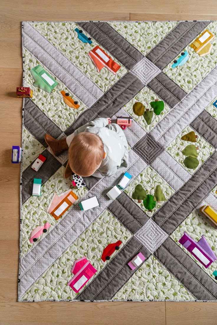 a baby laying on top of a quilted floor next to toy cars and trucks