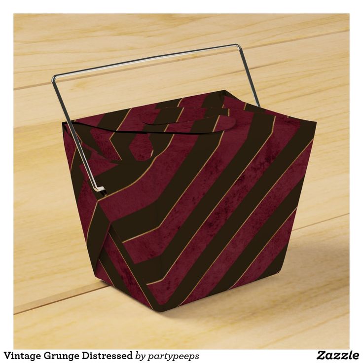 a red and brown striped box on a wooden floor with a metal handle that is attached to it