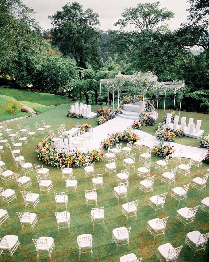 an outdoor ceremony setup with white chairs and flowers on the lawn, surrounded by greenery