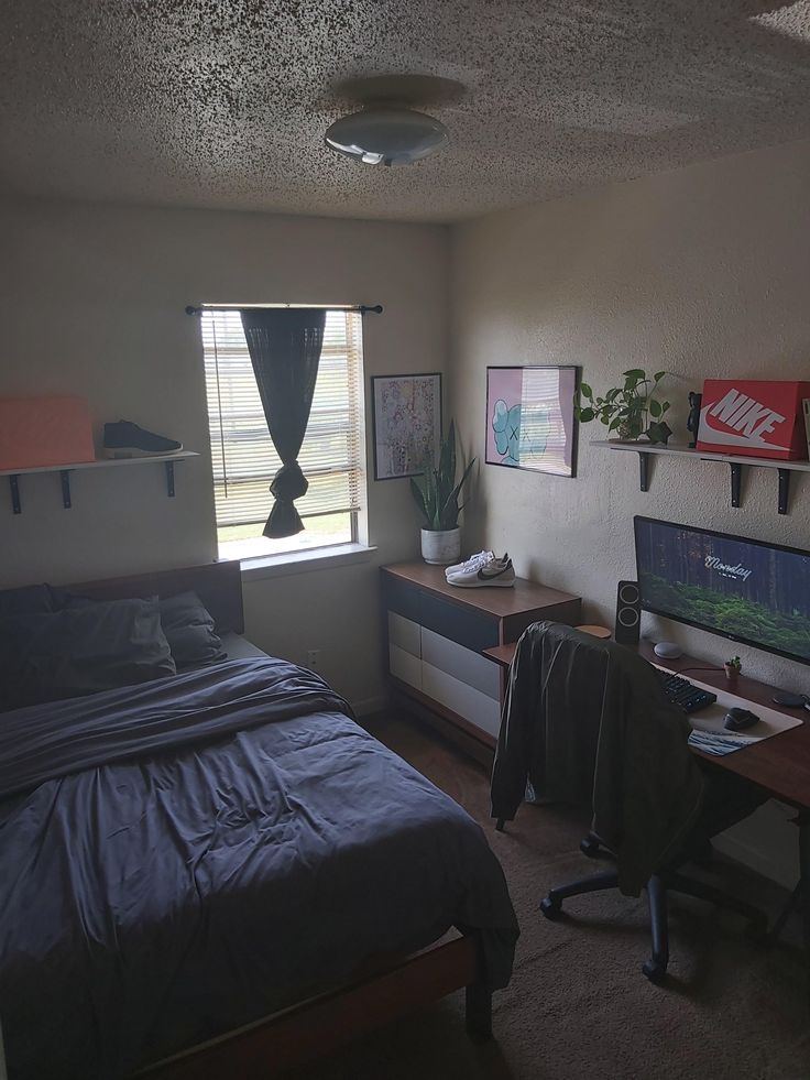 a bedroom with a bed, desk and computer monitor on the wall next to it