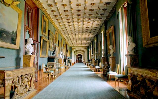 a long hallway with many paintings on the walls and ceiling, along with tables and chairs