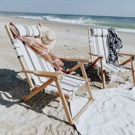 two beach chairs sitting on top of a sandy beach next to the ocean with towels draped over them