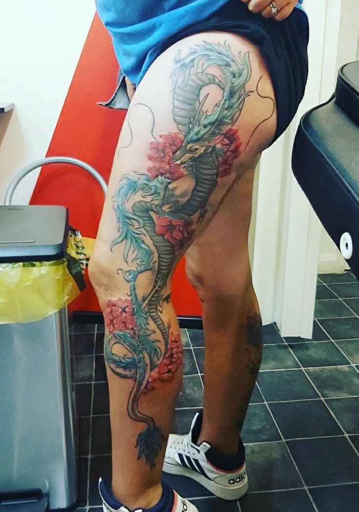 a person with a dragon tattoo on their thigh and leg, standing in front of a chair