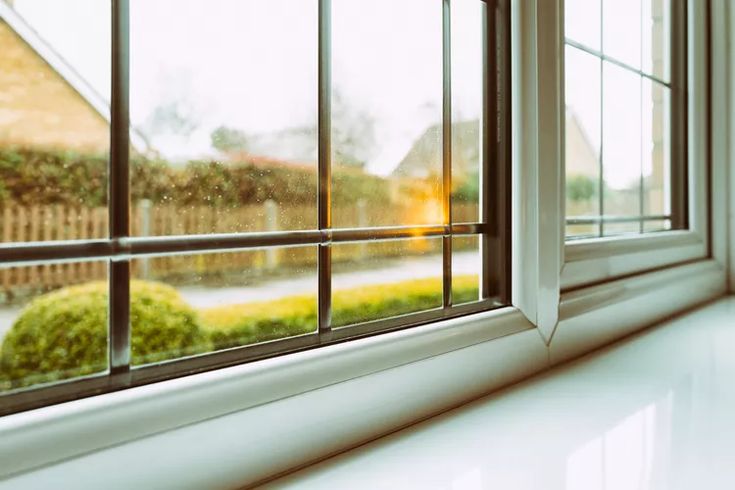 an open window with rain falling on the windowsill and green bushes in the background