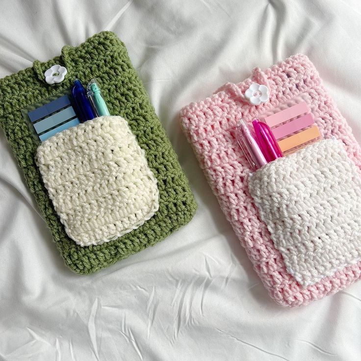 two crocheted purses with pens and pencils on them sitting on a bed