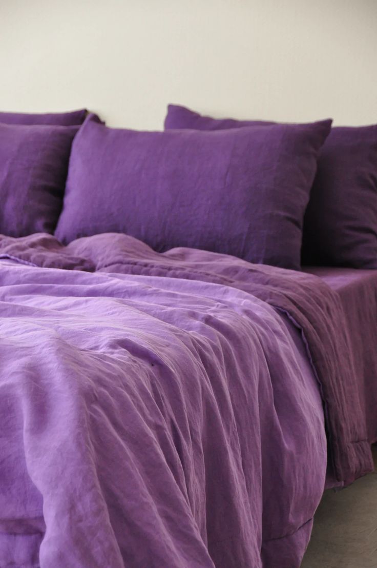 a bed covered in purple sheets and pillows