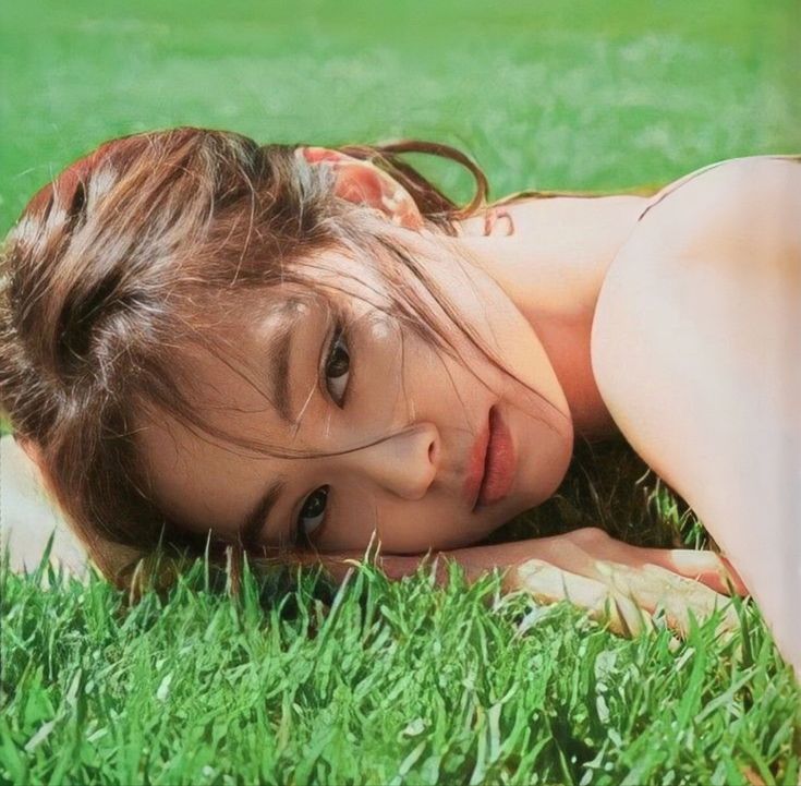 a woman laying in the grass with her head on her hand and eyes closed, looking at the camera