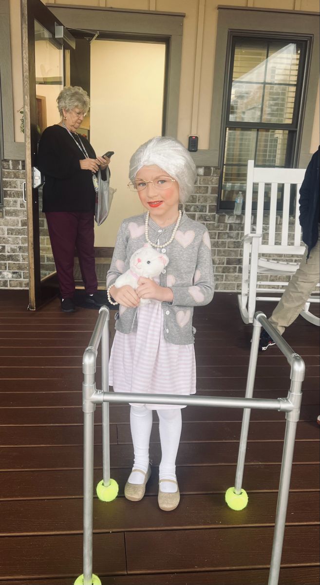 an older woman standing next to a white chair and holding a stuffed animal in her hand