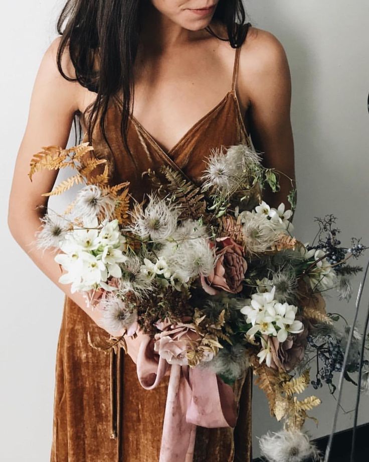 a woman holding a bouquet of flowers in front of her face and wearing a brown dress