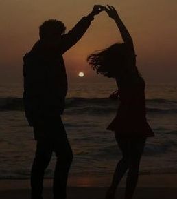 two people standing on the beach with their arms in the air and sunset behind them