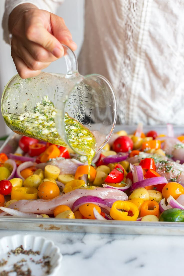 a person pouring dressing into a tray full of colorful peppers, onions and other vegetables