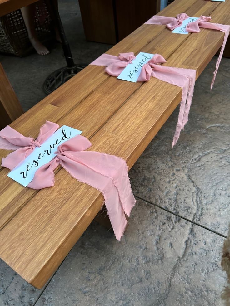 two wooden benches with pink ribbons tied to them and name tags attached to the sides