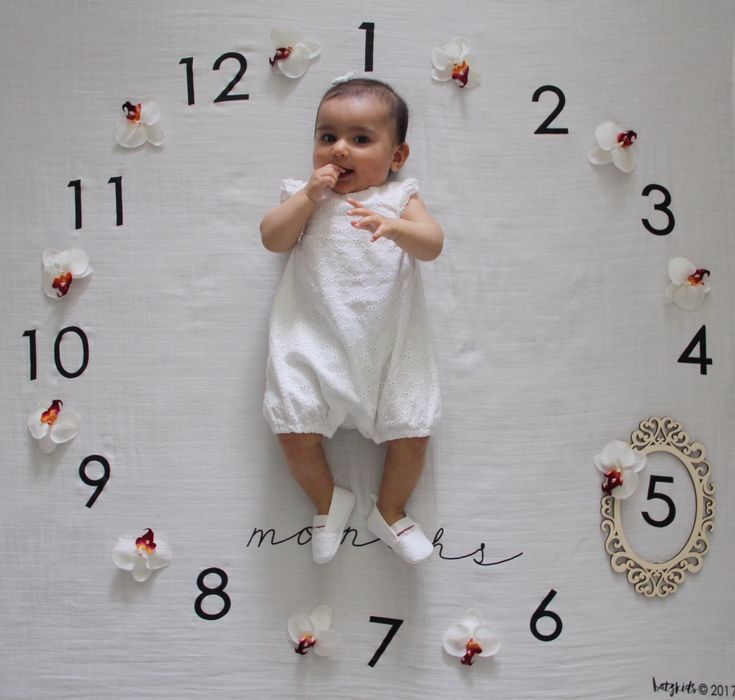 a baby is laying down in front of a clock