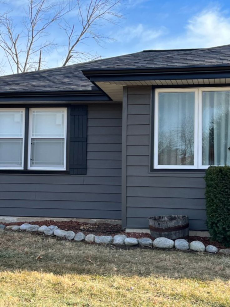 a gray house with white windows and bushes