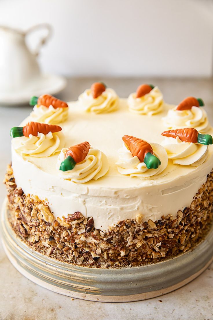 a carrot cake with white frosting and nuts on the top is sitting on a table