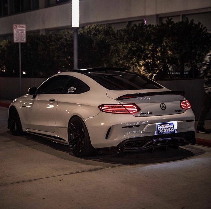 a white mercedes cla parked in front of a building at night with its lights on