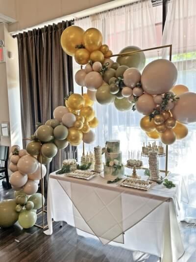 a table topped with lots of balloons next to a wall covered in gold and white