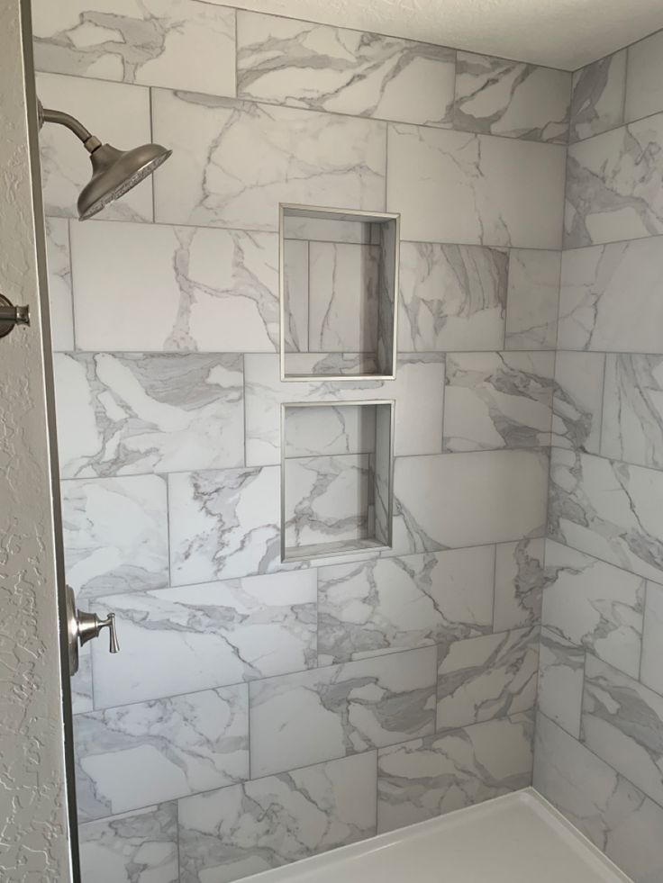 a bathroom with white marble walls and tile flooring, shower head, and window in the corner