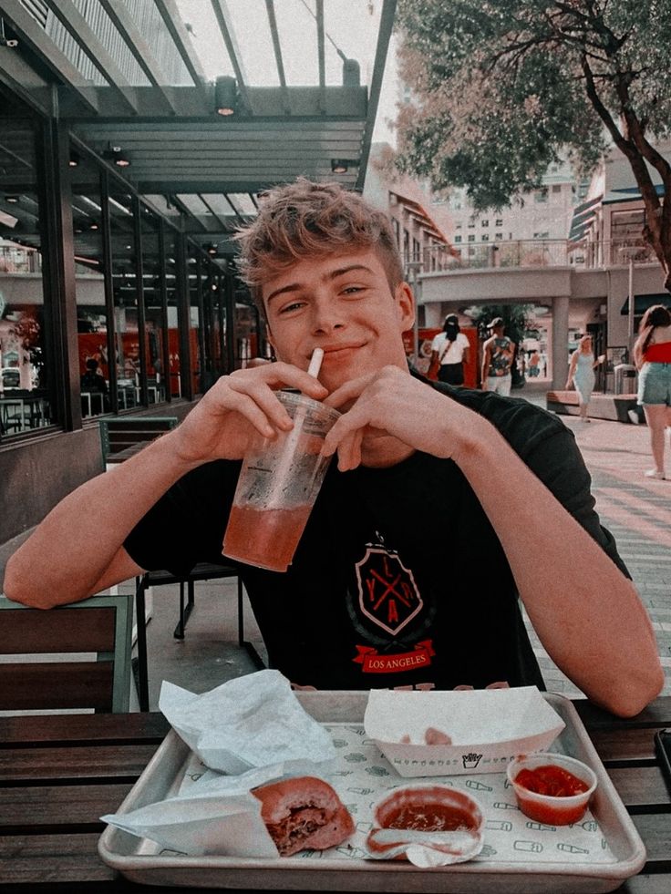 a young man sitting at a table with food and drink in front of his face