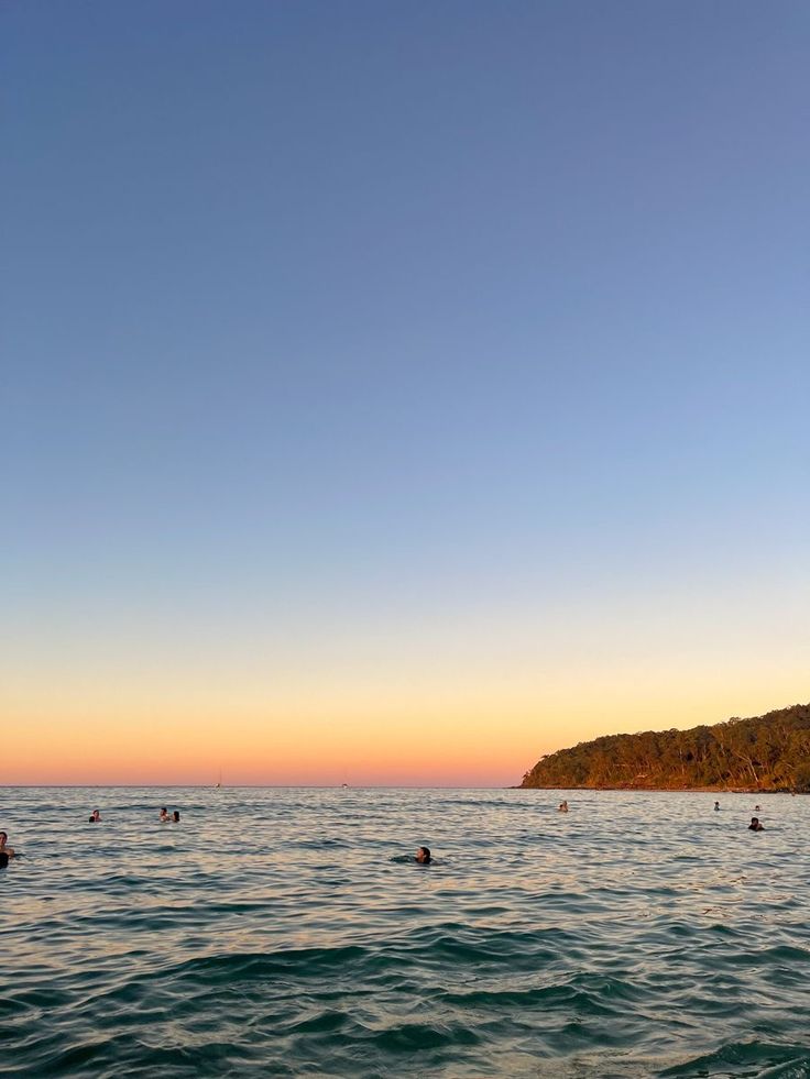 people swimming in the ocean at sunset