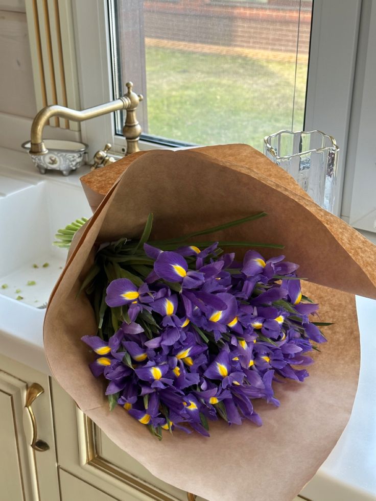 a bouquet of purple flowers sitting on top of a kitchen sink