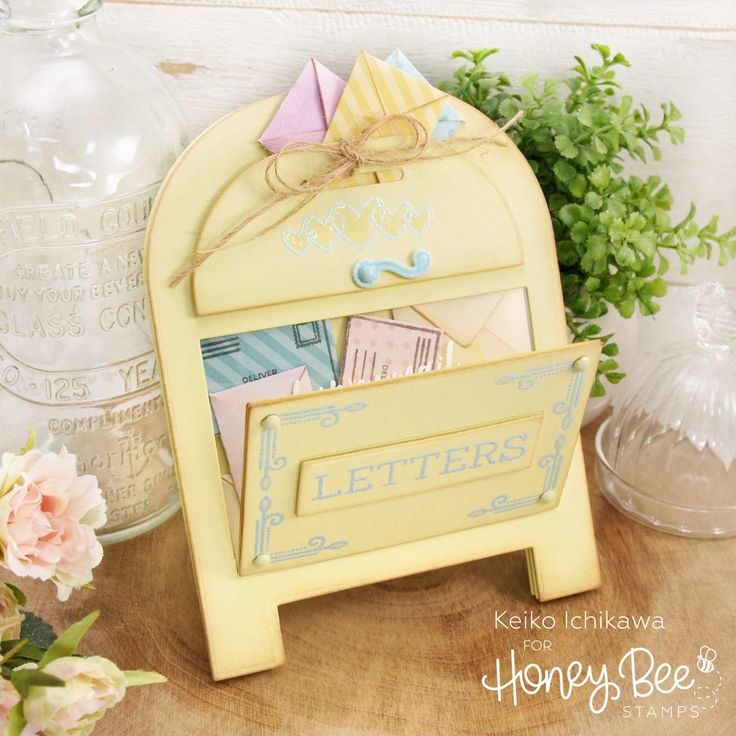 a yellow mailbox sitting on top of a wooden table next to vases and flowers