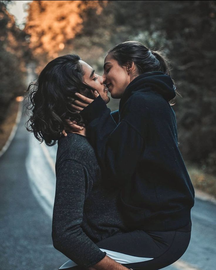 two women kissing on the side of a road with trees in the backgroud