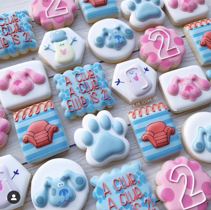 decorated cookies with blue and pink icing are arranged on a white tablecloth that is laid out