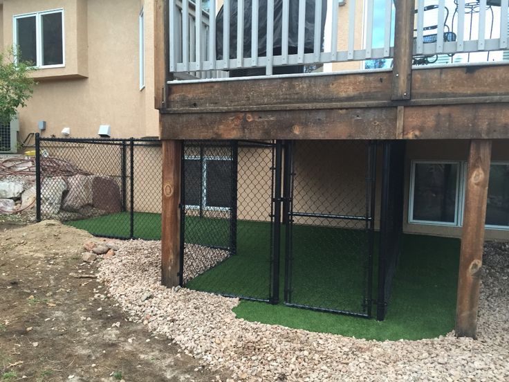 a dog kennel in front of a house with grass and rocks on the ground