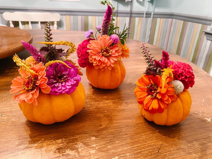 three pumpkins decorated with flowers sit on a table