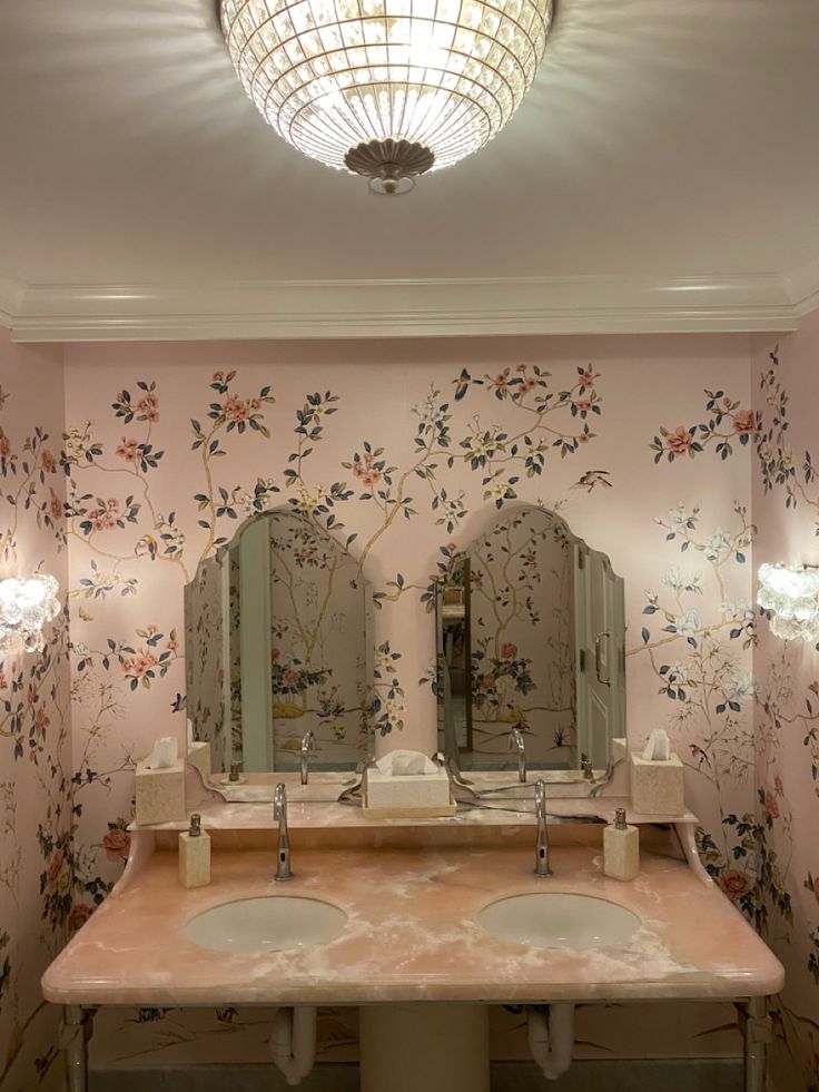 two sinks and mirrors in a bathroom with floral wallpaper on the walls behind them